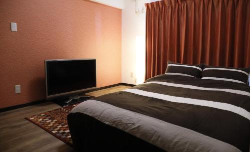 a bedroom with a bed and a flat screen tv at ケイアイコンホテルズ 池下 in Chikusachō