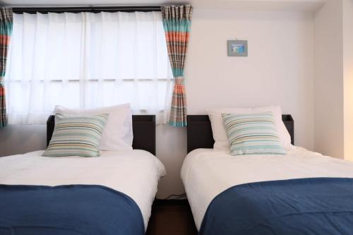 two beds in a room with a window at ケイアイコンホテルズ 池下 in Chikusachō