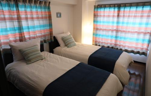 two beds in a room with windows and curtains at ケイアイコンホテルズ 池下 in Chikusachō