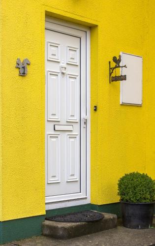a yellow building with a white door and a sign at Mount Brandon Cottages Graiguenamanagh in Graiguenamanagh