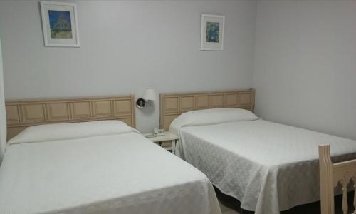 two beds in a room with white sheets at Hostal Antolín in Redondela