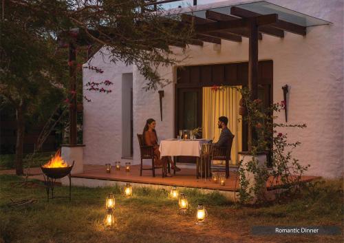 a man and woman sitting at a table next to a fire at The Serai Bandipur in Bandipūr