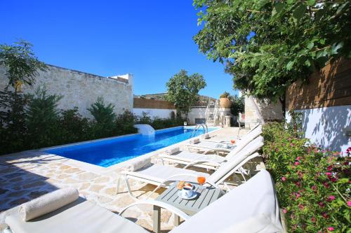 a pool with white lounge chairs next to a building at Villa Oasis in Kamilari