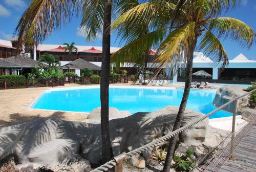 a swimming pool with two palm trees next to a resort at L'Escale - vue mer avec cuve in Saint-François
