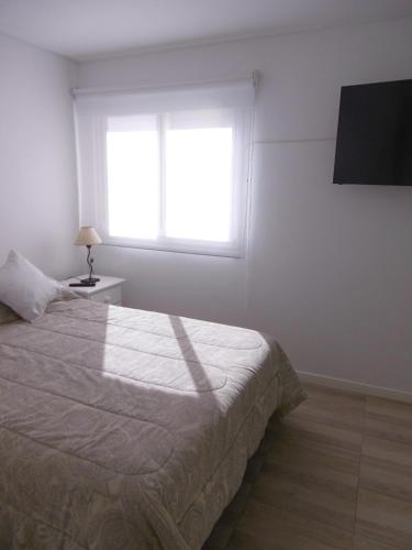 a white bedroom with a bed and a window at DEPTOS VIP en EDIFICIO FRENTE AL MAR-ZONA CONSTITUCION in Mar del Plata