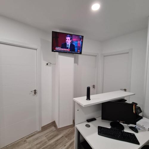 a room with a desk with a computer and a tv on the wall at Hostal Las Fronteras in Torrejón de Ardoz