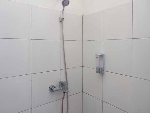 a shower in a white tiled bathroom with a hose at RedDoorz near RSUD Nganjuk in Nganjuk