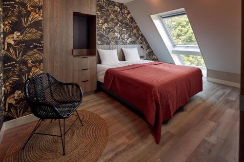 Farm house Van der Valk Hotel Leeuwarden في ليوواردن: غرفة نوم بسرير وبطانية حمراء وكرسي
