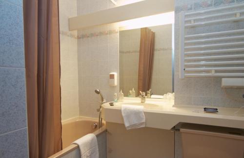 a bathroom with a sink and a mirror and a tub at Hotel Sully in Nogent-le-Rotrou