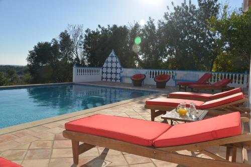 - une piscine avec des chaises rembourrées de couleur rouge et une table à côté dans l'établissement Quinta da Fonte em Moncarapacho, à Moncarapacho