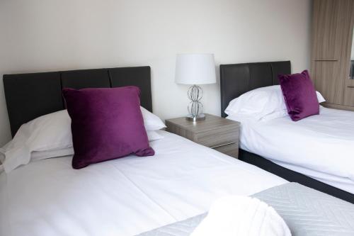 two beds with purple pillows in a hotel room at Friarscroft Lodge Holiday Home in Wymondham