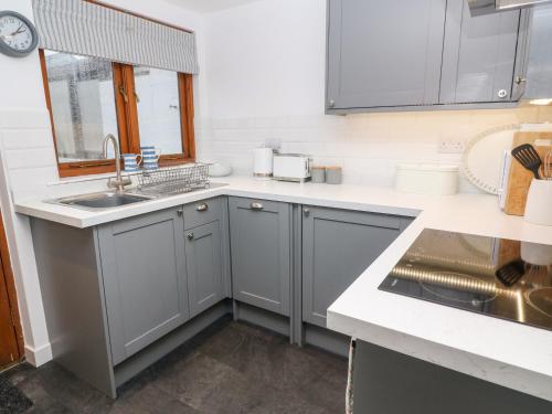 uma cozinha com armários cinzentos e um lavatório em Miners Cottage em Penzance