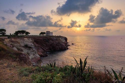a sunset over the ocean with a house on a cliff at Casa Manzella in Terrasini