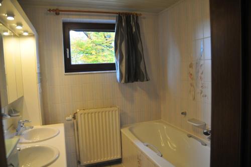 baño con bañera, 2 lavabos y ventana en La Maison du Bonheur en Gouvy