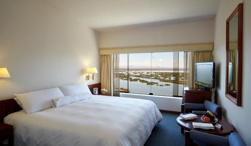 ein Hotelzimmer mit einem großen Bett und einem großen Fenster in der Unterkunft GHL Hotel Lago Titicaca in Puno