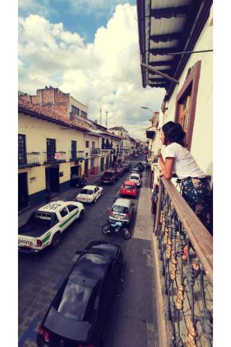 a woman standing on a balcony looking at a street with cars at Hostal Yakumama in Cuenca
