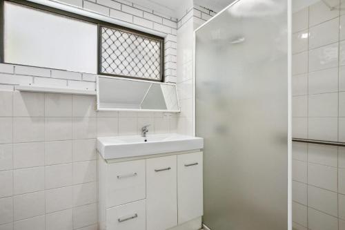 a white bathroom with a sink and a window at Golden Shores Unit 1 21 Landsborough Parade in Caloundra