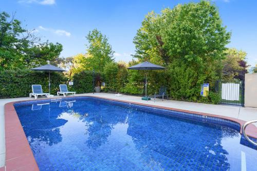 a swimming pool with two chairs and two umbrellas at Beechworth Motor Inn in Beechworth