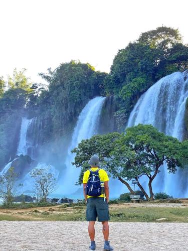 a man with a backpack standing in front of a waterfall at Yen Nhi Homestay Ban Gioc in Cao Bằng