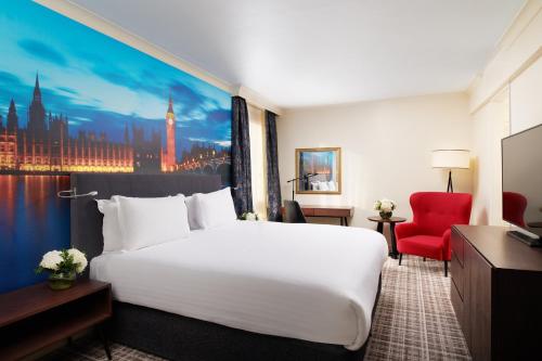 ロンドンにあるミレニアム グロスター ホテル ロンドンの白い大型ベッドと赤い椅子が備わるホテルルームです。