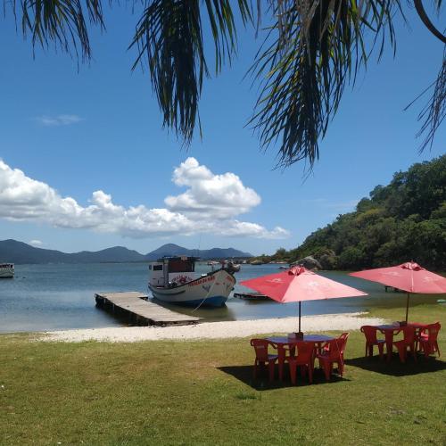 two tables and umbrellas on a beach with a boat at Joaquina 433 - Pousada Floripa in Florianópolis