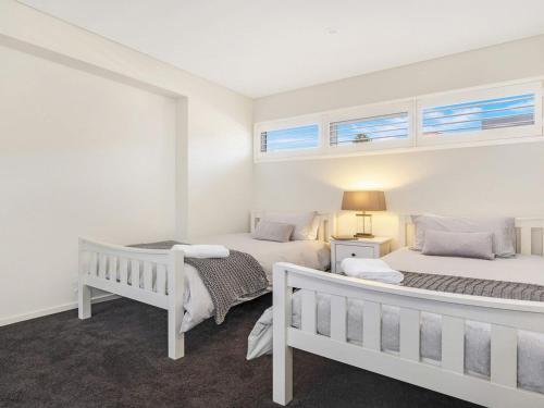 two beds in a bedroom with white walls and windows at Bathers at the Beach in Kiama