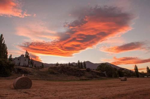 a field with hay bales in front of a sunset at Gibbston Boathouse with Outdoor Bath in Gibbston