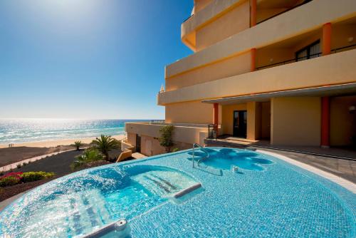 a swimming pool in front of a building with the ocean at Iberostar Waves Playa Gaviotas All Inclusive in Morro del Jable