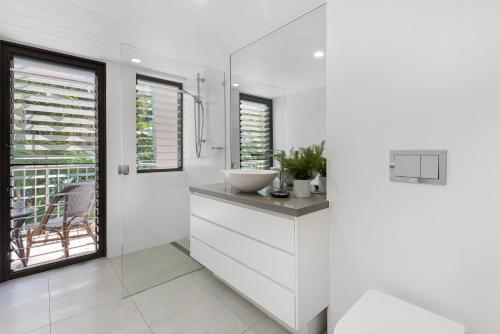 La salle de bains blanche est pourvue d'un lavabo et d'un miroir. dans l'établissement Naousa II Apartment 5, Little Cove, à Noosa Heads