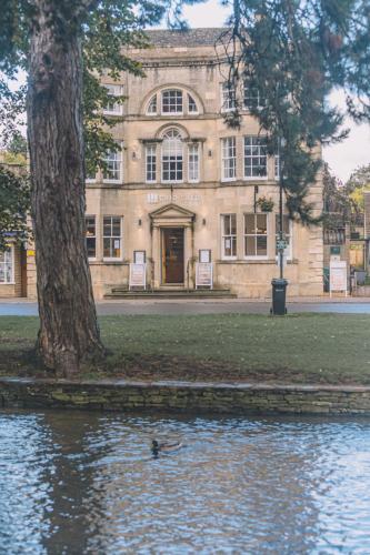 a building with a tree in the middle of a body of water at Old Bank Rooms in Bourton on the Water