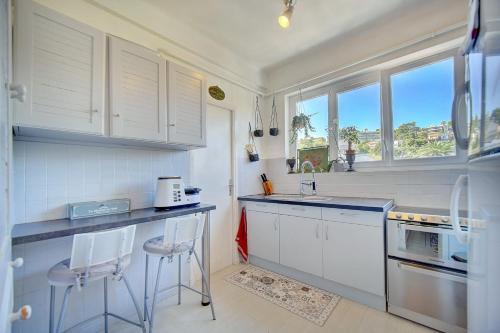 une cuisine avec des placards blancs et un comptoir avec deux tabourets dans l'établissement IMMOGROOM - Close beaches- Beautiful terrace - Seaview - CONGRESSBEACHES, à Cannes