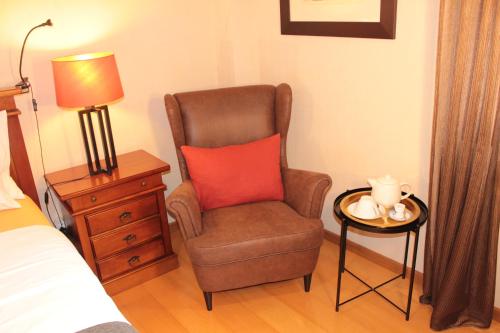 a bedroom with a chair with a red pillow and a table at Cosy Rooms in Sacavém