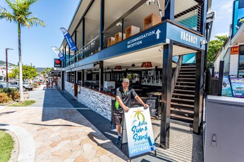 a woman holding a sign in front of a store at Airlie Sun & Sand Accommodation Studio #1 in Airlie Beach