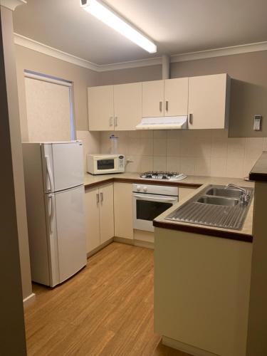 a kitchen with white cabinets and a white refrigerator at Waratah in Albany