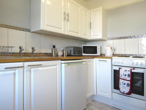 una cocina con armarios blancos y electrodomésticos blancos en Wickham House Apartment, en Fremington