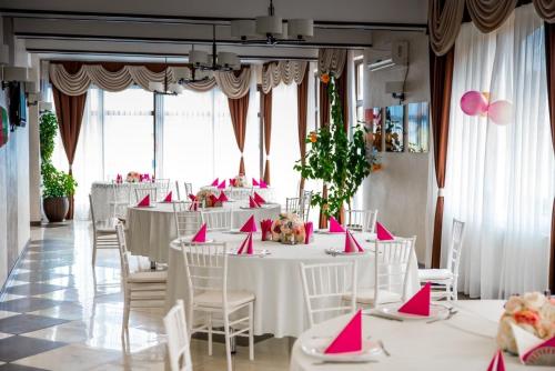 un salón de banquetes con mesas blancas y servilletas rosas en Pensiunea Luminita, en Târgu Jiu