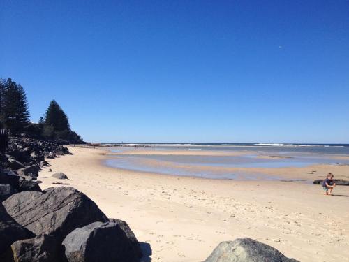 a person walking on a beach with rocks at XYL Holiday Inn in Caloundra