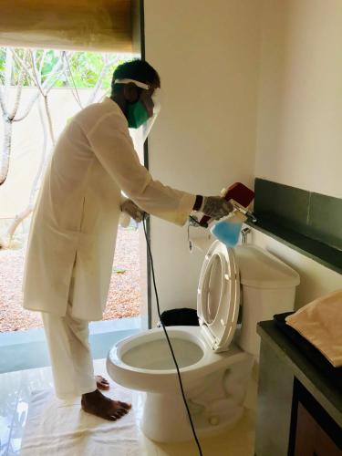 a man in a mask is washing a toilet at Shreyas Retreat in Nelamangala
