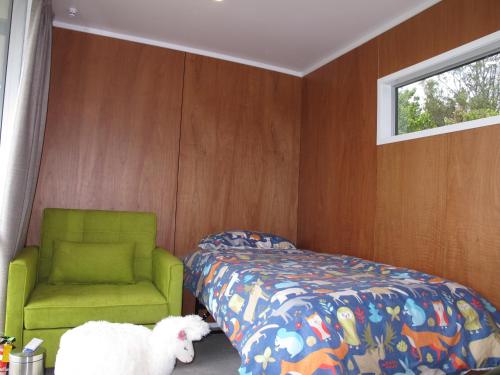 a bedroom with a bed and a green chair at Waihi Gold Alpacas 3 or 4 people in Waihi