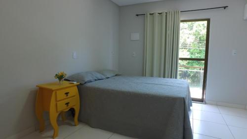 a bedroom with a bed with a nightstand and a window at Residencial Zé Buscapé in Bombinhas