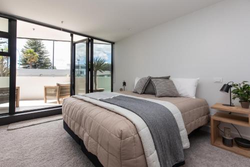 a bedroom with a large bed and a large window at Ocean Eleven Deluxe in Mount Maunganui