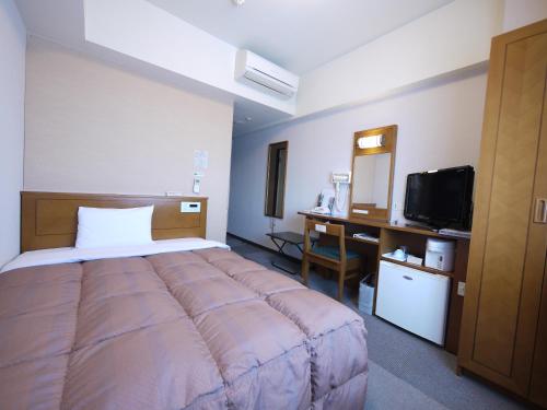 a bedroom with a bed and a desk and a television at Hotel Route-Inn Matsusaka Ekihigashi in Matsuzaka