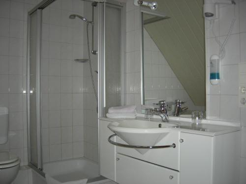La salle de bains blanche est pourvue d'un lavabo et d'une douche. dans l'établissement Bastan - Haus Katharina, à Emden