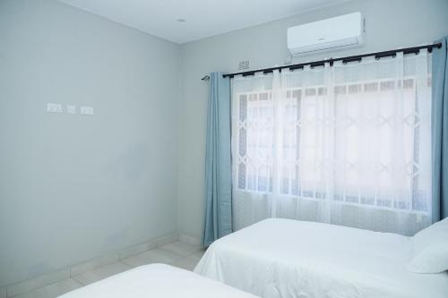a white bedroom with two beds and a window at Greyville Apartments in Lusaka