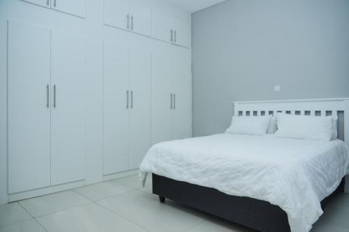 a white bedroom with a bed with white sheets and pillows at Greyville Apartments in Lusaka