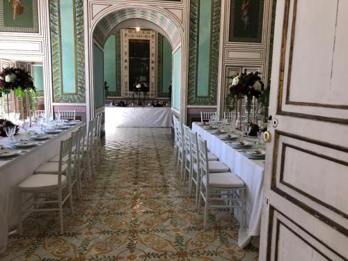 une rangée de tables dans une pièce avec des chaises et des supports mobiles dans l'établissement Landolina Palace Hotel, à Noto