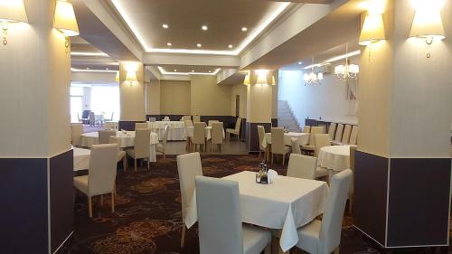 uma sala de jantar com mesas brancas e cadeiras brancas em Hotel Story em Târgu Jiu