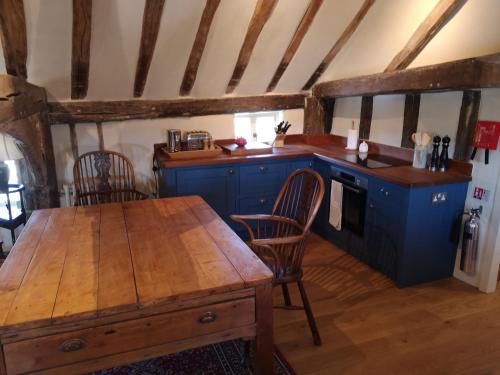 cocina con armarios azules y mesa de madera en The Queen's Head en Hawkedon