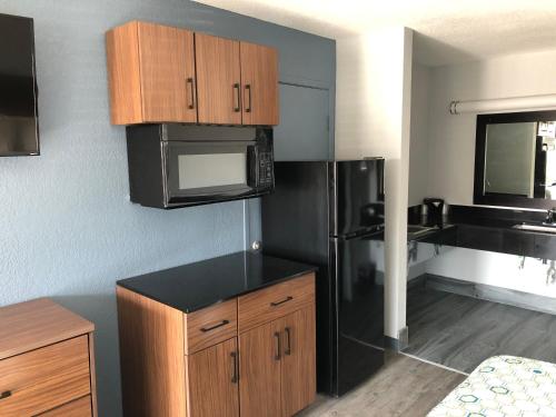 Una cocina con refrigerador negro y gabinetes de madera. en HomeTowne Studios by Red Roof San Antonio E - Frost Bank Center, en San Antonio