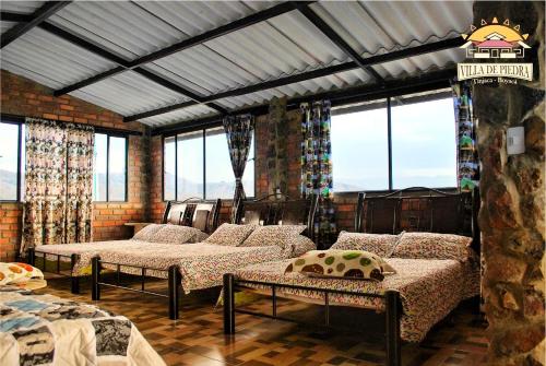 a room with two beds and windows with windows at Hospedaje Villa de piedra in Tinjacá